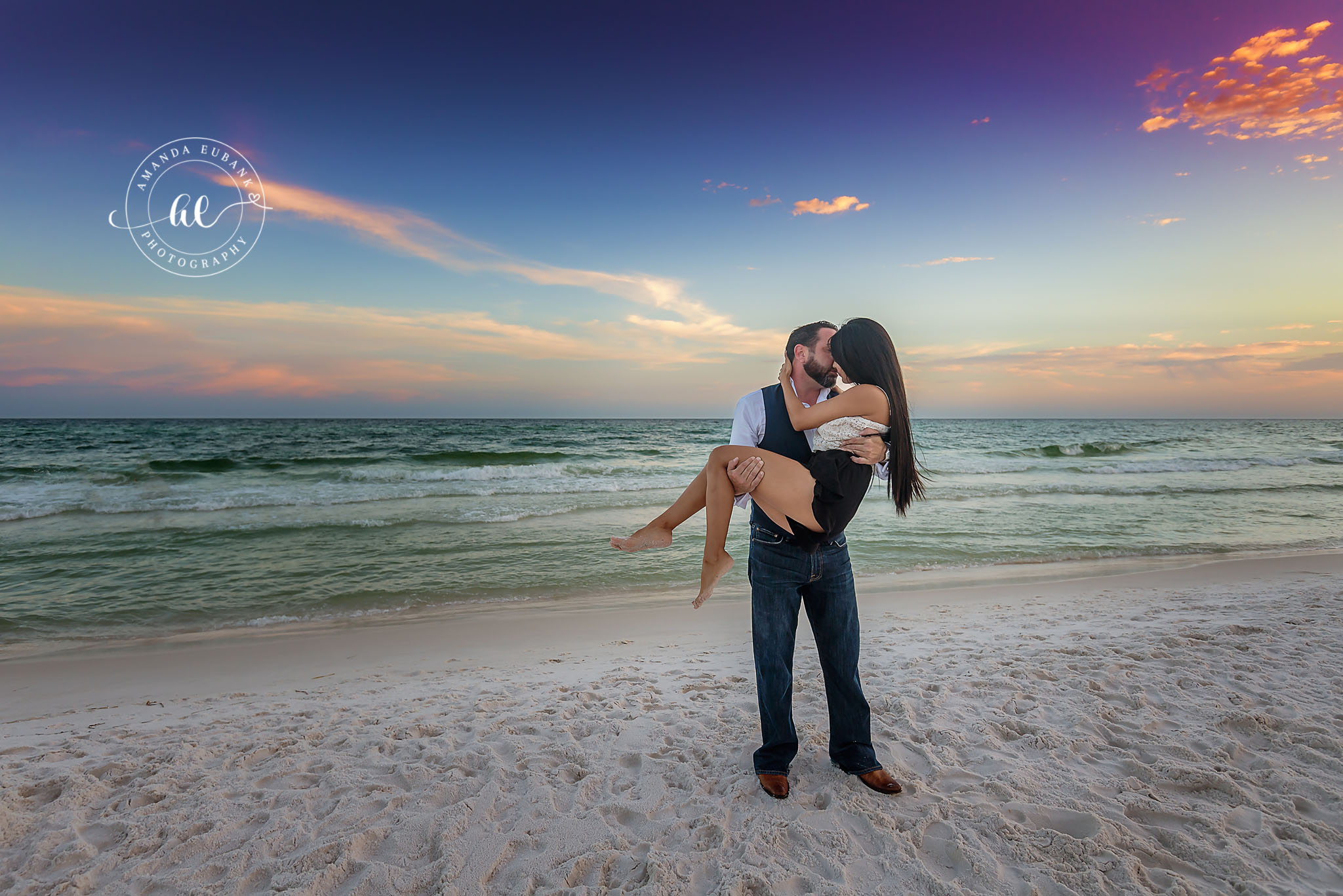 Seaside engagement photographer captures groom carrying bride-to-be on the beach at sunset