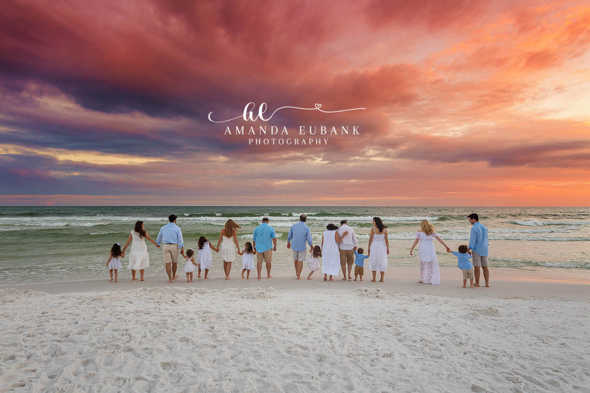 Seaside family photographer captures large extended family holding hands at water edge at fiery sunset