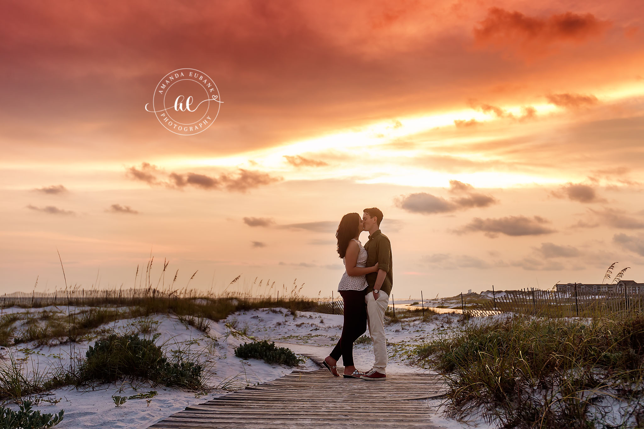 Seaside engagement photographer captures couple kissing on beach boardwalk at sunset