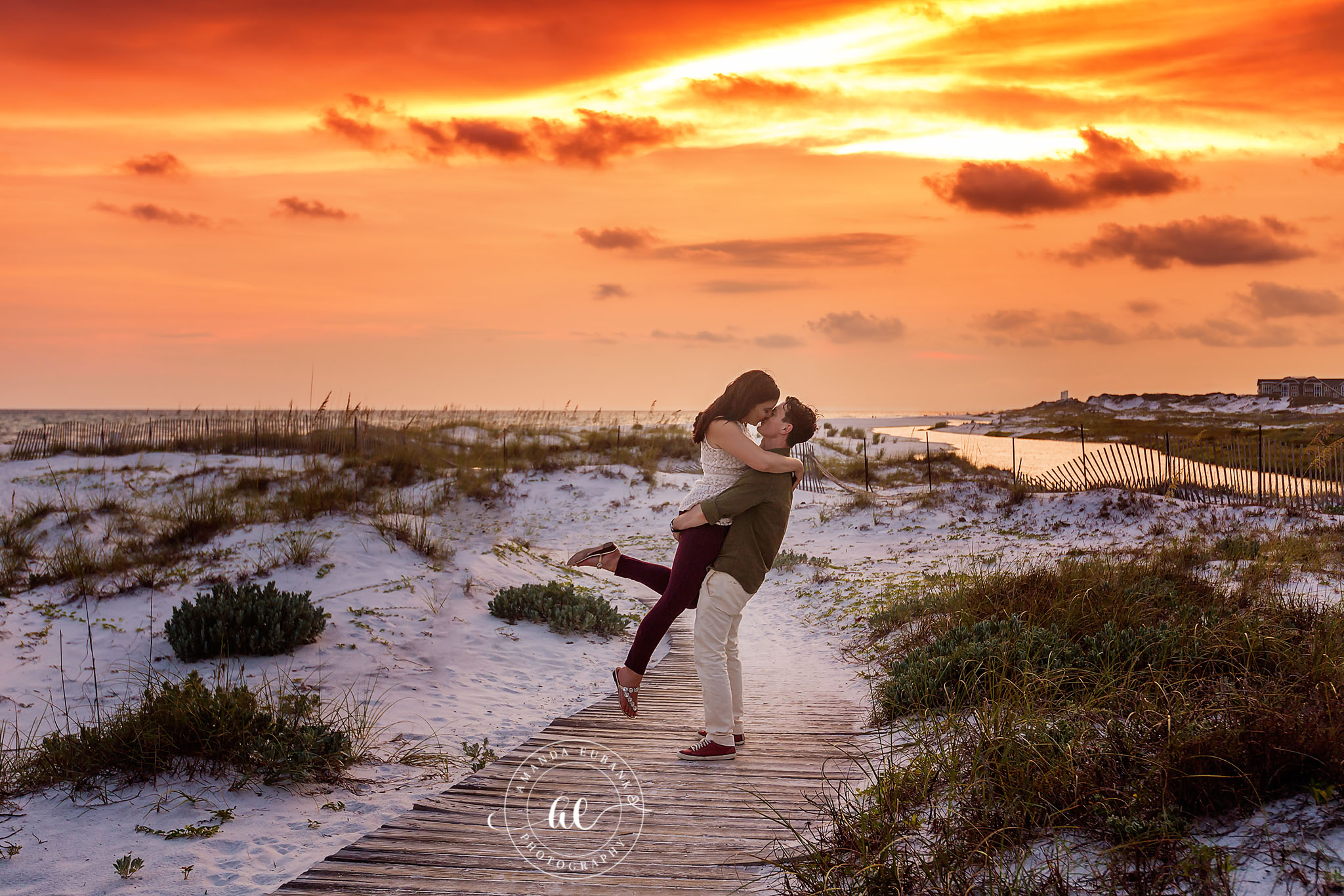 Seaside engagement photographer captures joyful lift on beach boardwalk at golden sunset