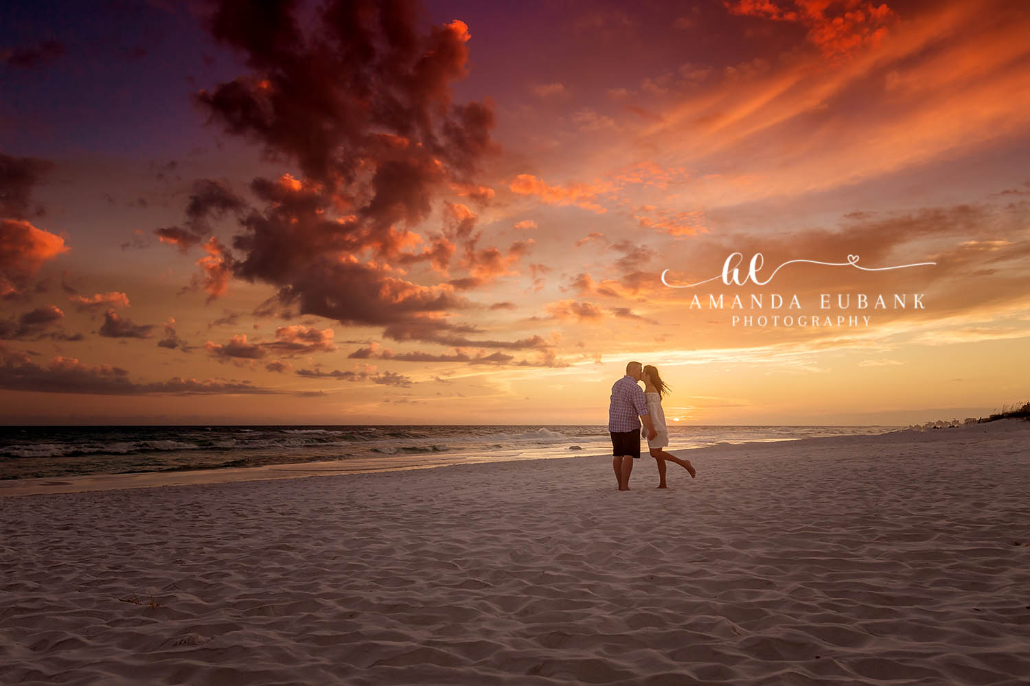 Seaside engagement photographer captures couple silhouetted against vibrant orange sunset on beach