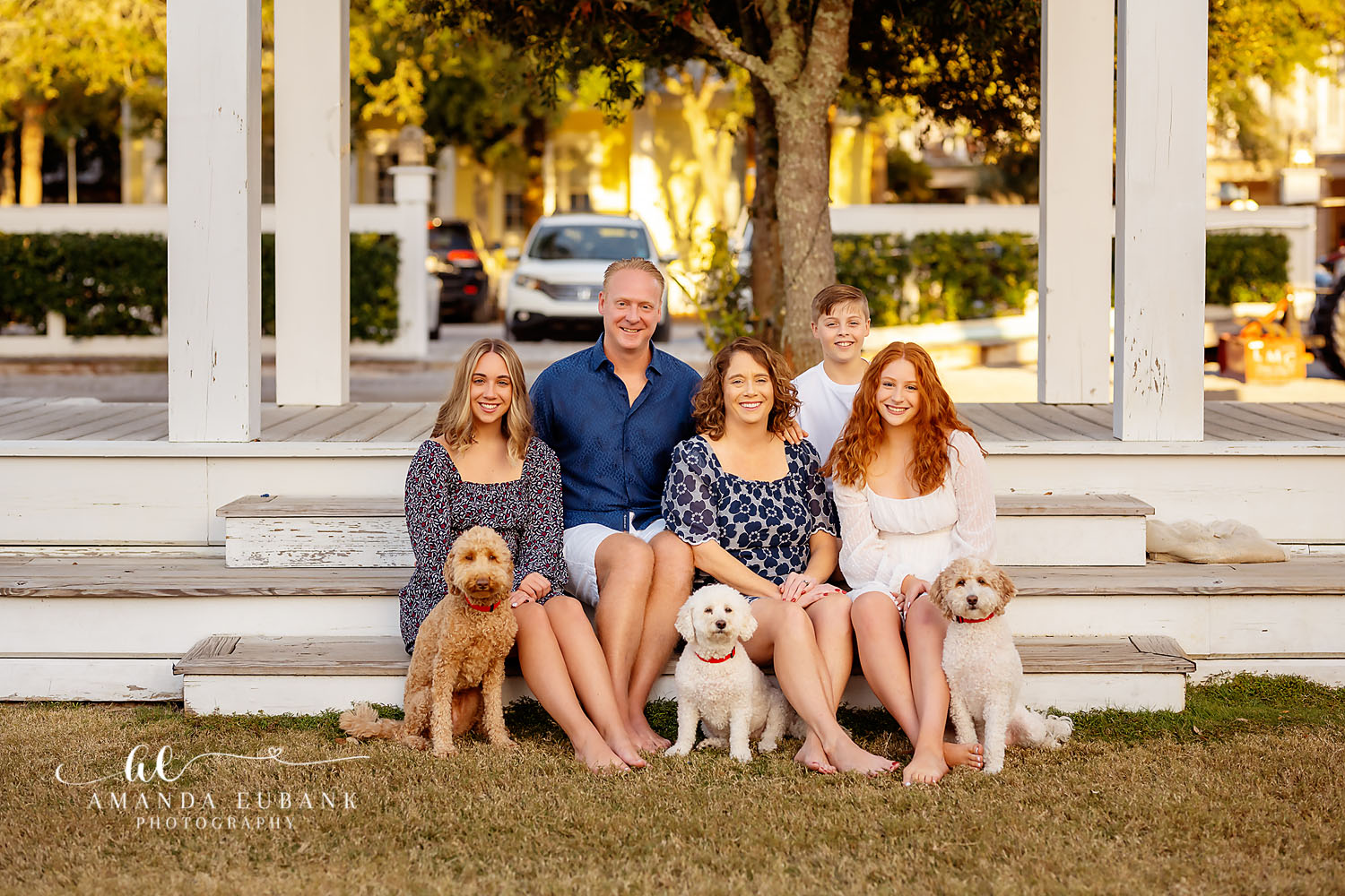 Family of five with three golden doodle dogs sitting on white cottage porch steps in Seaside Florida