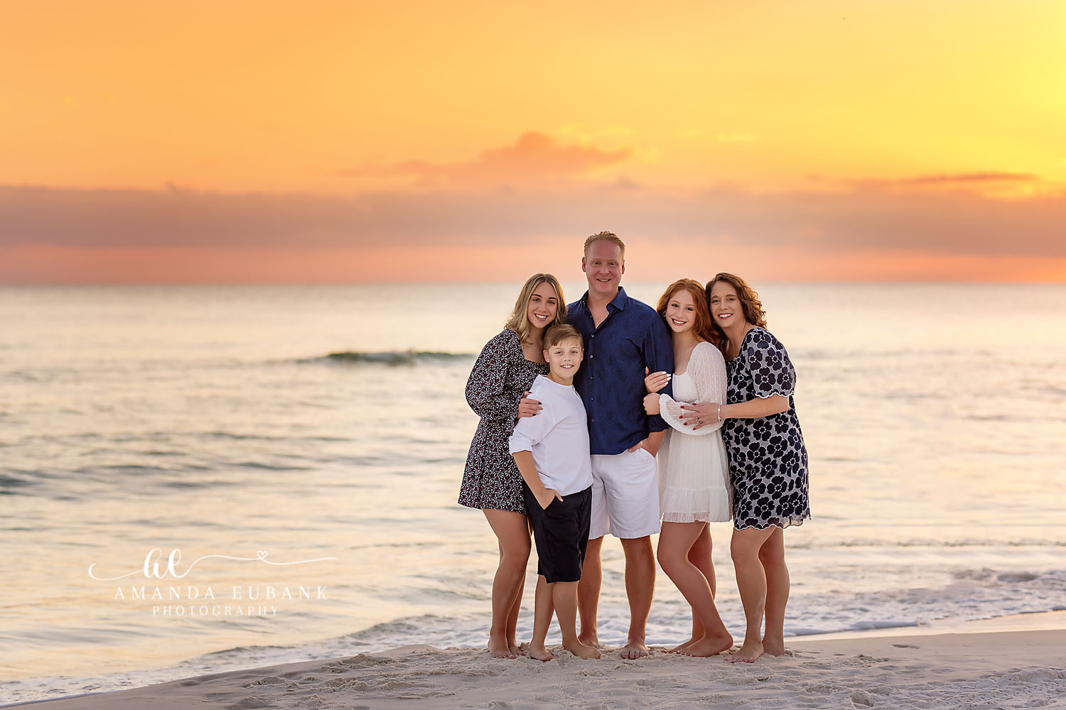 Family group sitting together on the beach at a golden pastel sunset in Seaside Florida