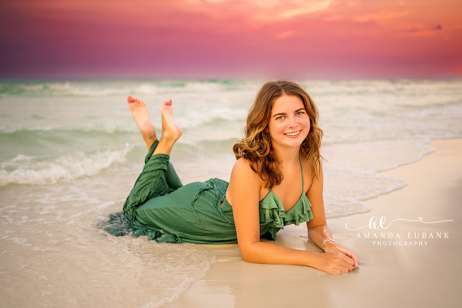 Seaside Florida senior photographer captures senior in green dress lying on beach at pink sunset