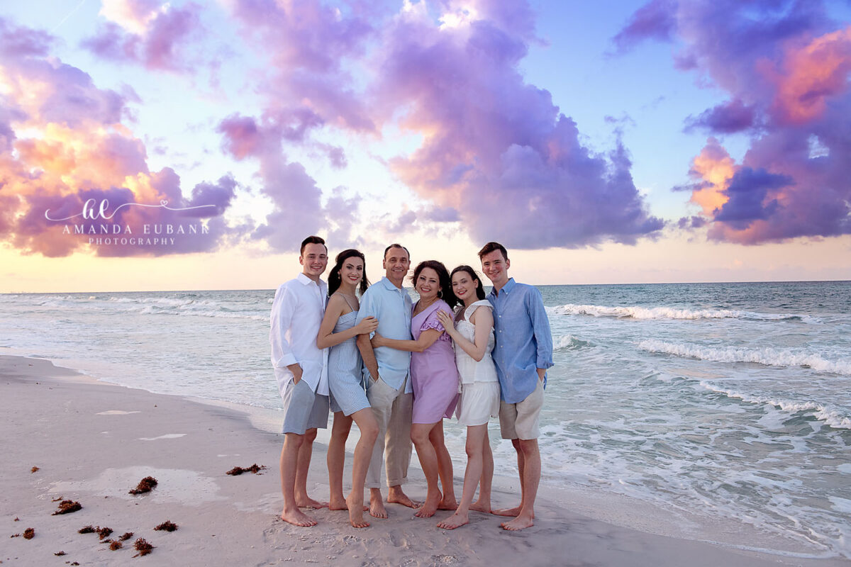 Family of five young adults and parents hugging together on the beach at a purple orange and pastel sunset in Seaside Florida