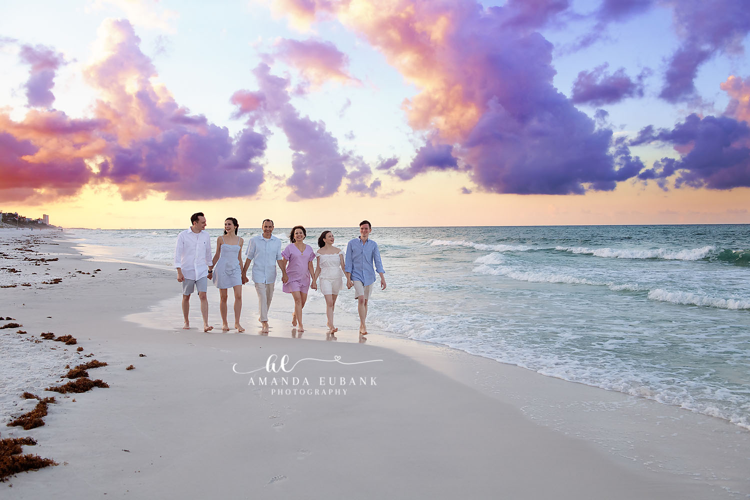 Family of six walking together along the shoreline at a purple and pink pastel sunset in Seaside Florida