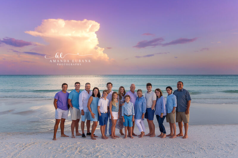 Large multigenerational family group of about 14 people posing on the beach at a dramatic purple and pink sunset in Seaside Florida
