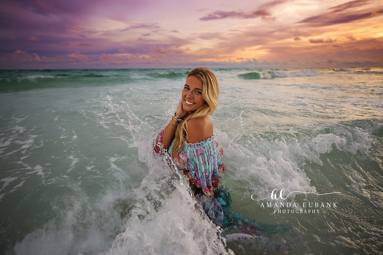 Seaside senior photographer captures blonde in tie-dye dress laughing in crashing surf at sunset