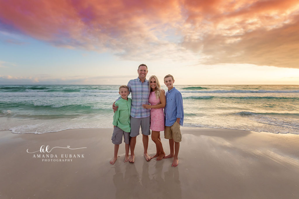 Family of Four Beach Portrait in Seaside Florida at Colorful Sunset Family of four smiling together on the beach with a stunning pink and orange sunset sky in Seaside Florida
