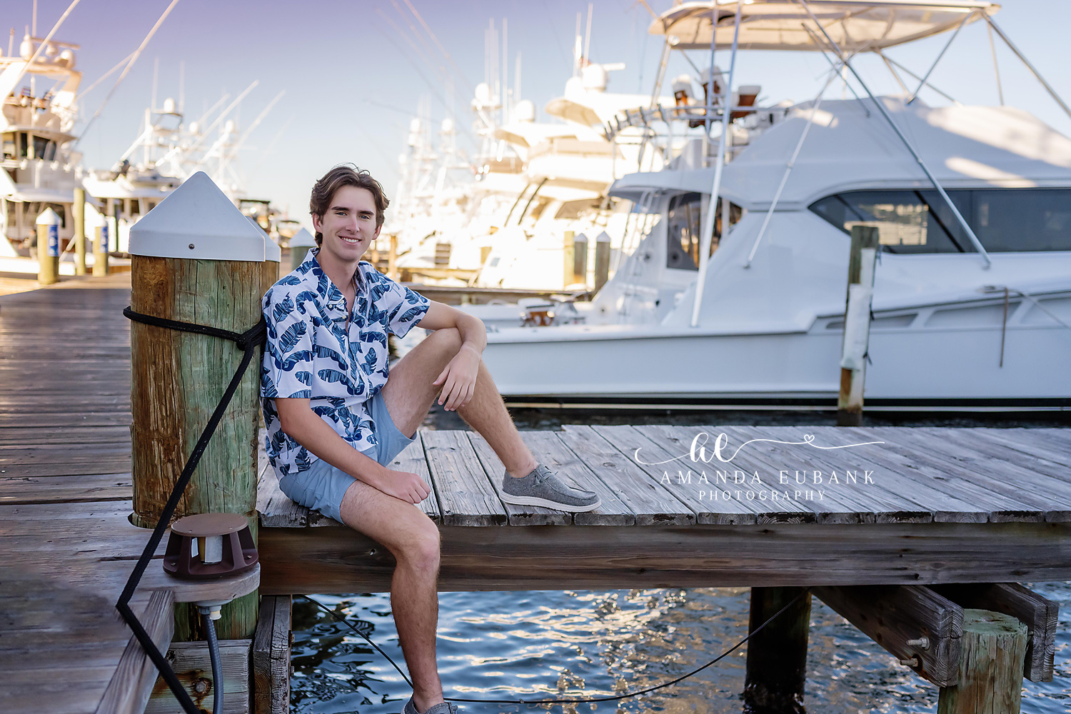 Seaside senior photographer captures male senior in tropical shirt seated on marina dock with yachts