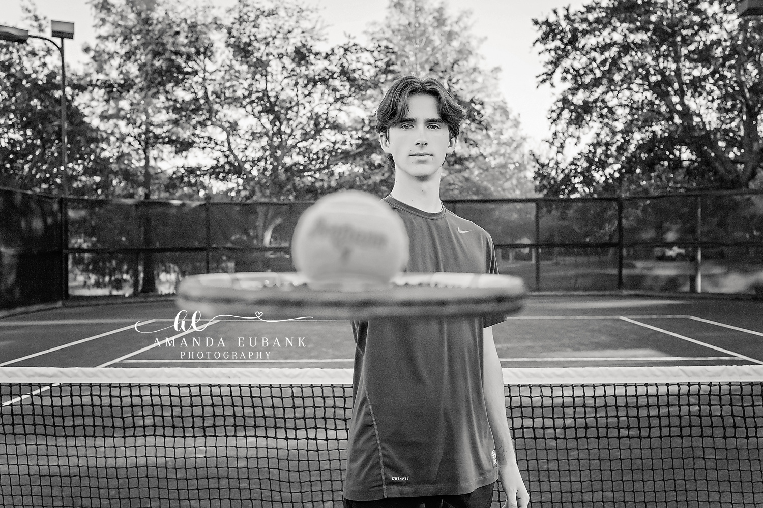 Seaside senior photographer captures male senior with tennis racket on court in black and white