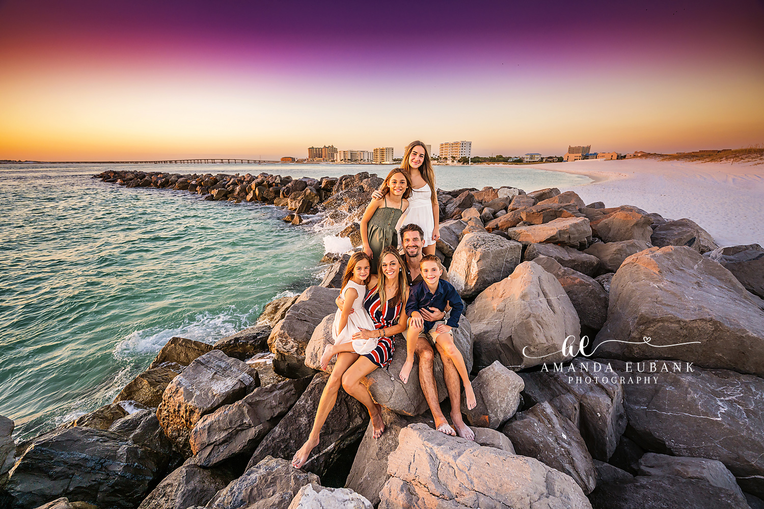 Seaside family photographer captures family of six on harbor jetty at vibrant split sky sunset