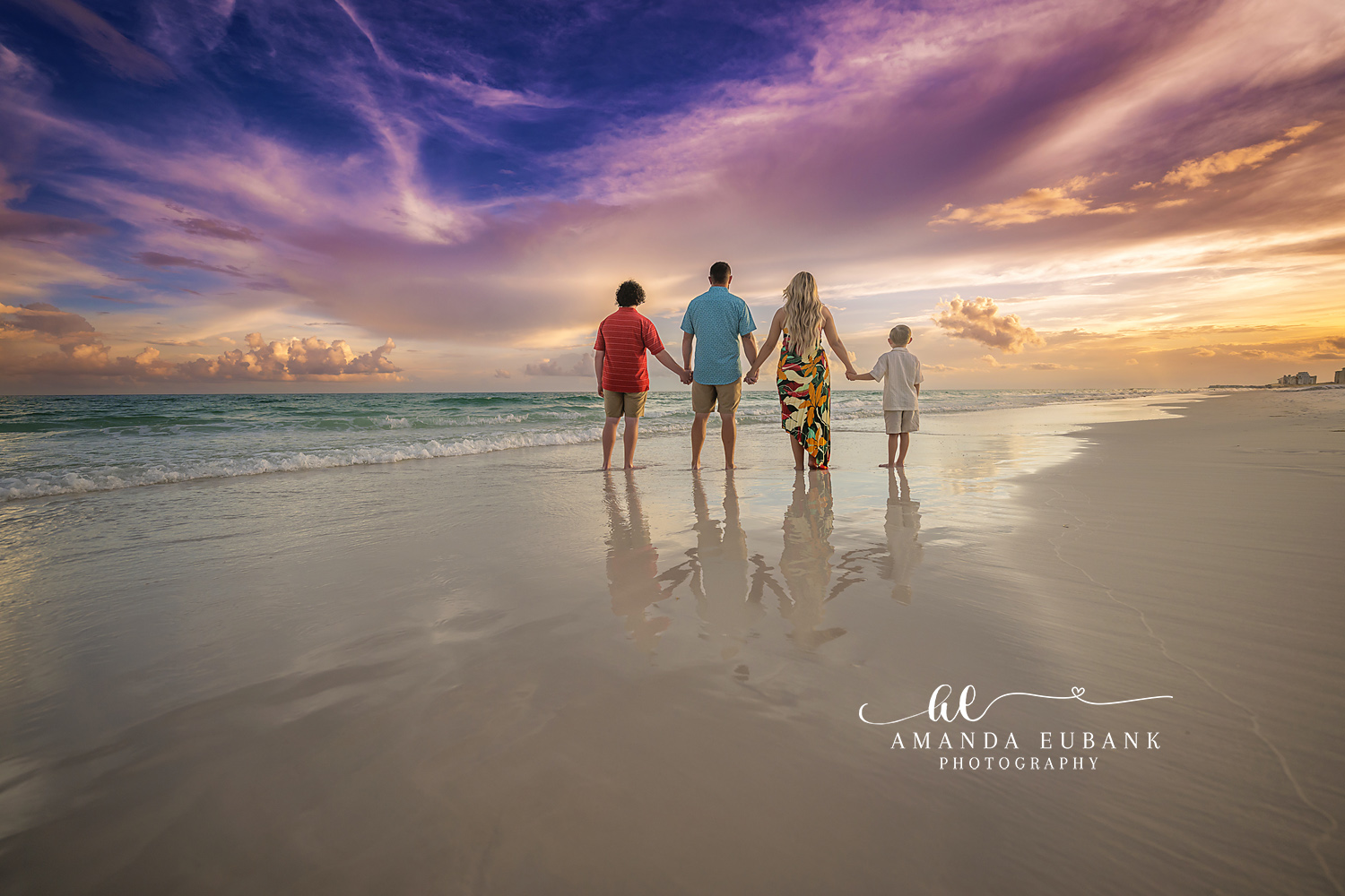 Seaside family photographer captures family of four walking into surf at purple sunset