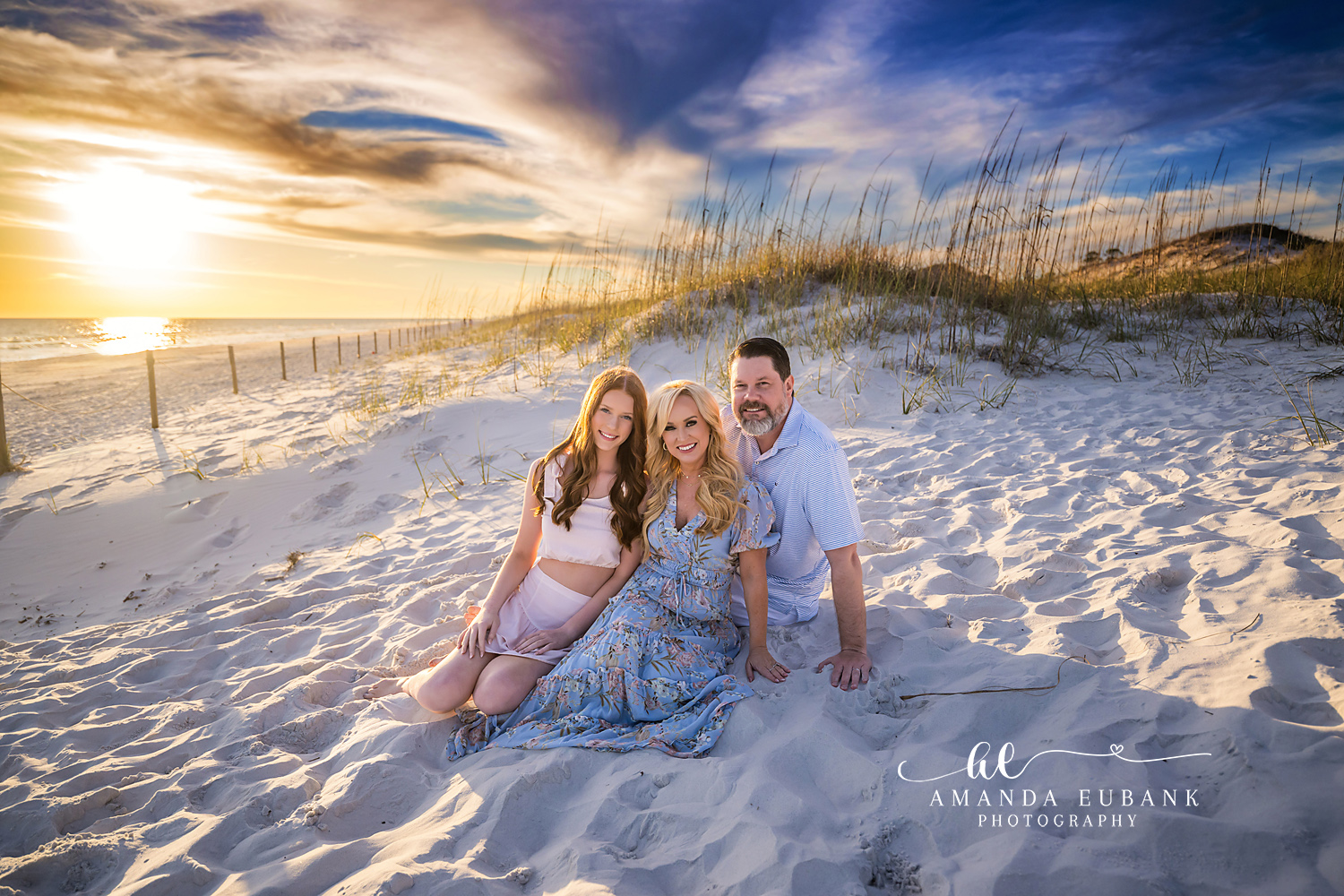 Seaside family photographer captures family of three by sea oat dunes at golden hour