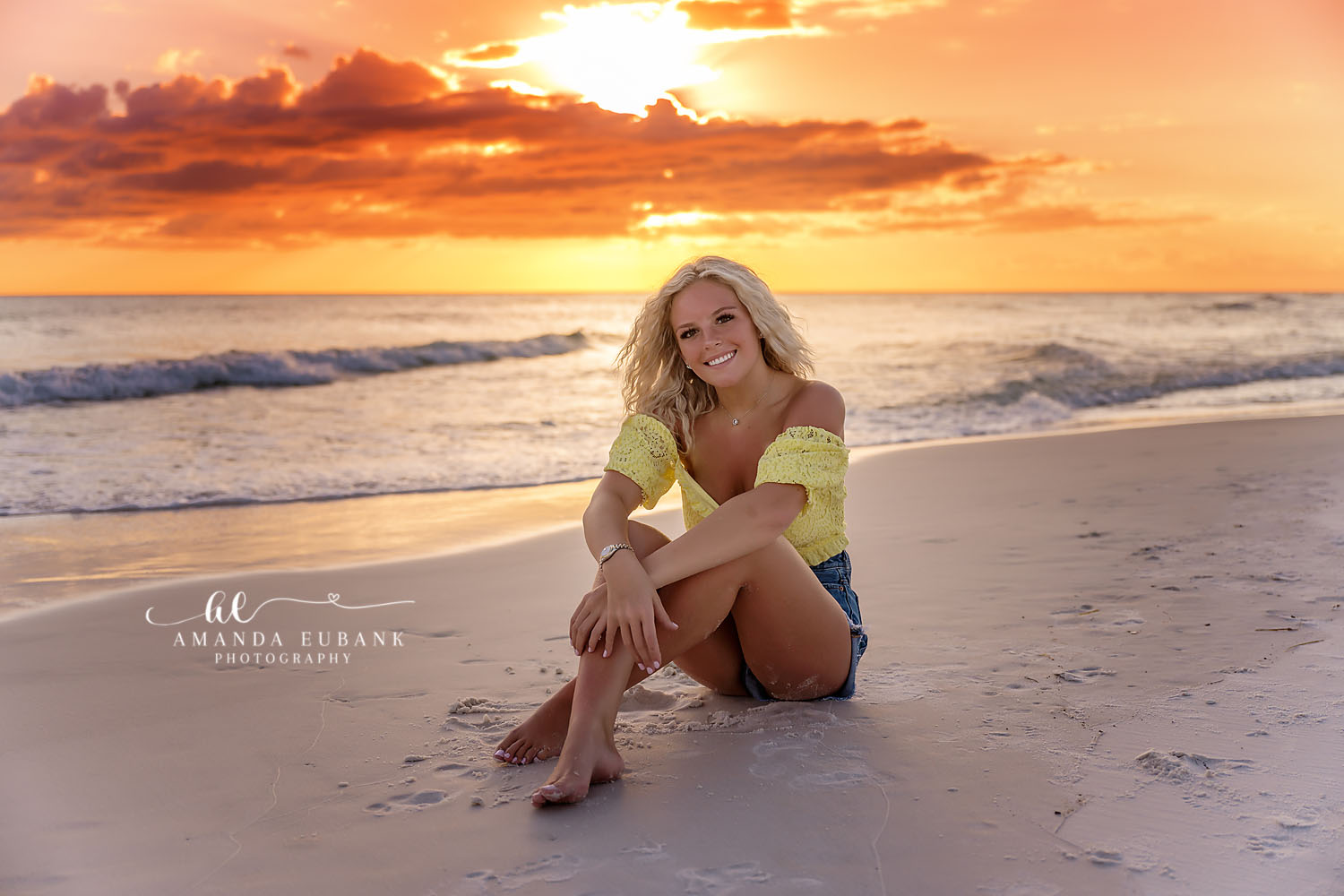 Seaside senior photographer captures smiling blonde senior on beach in yellow lace top at golden sunset