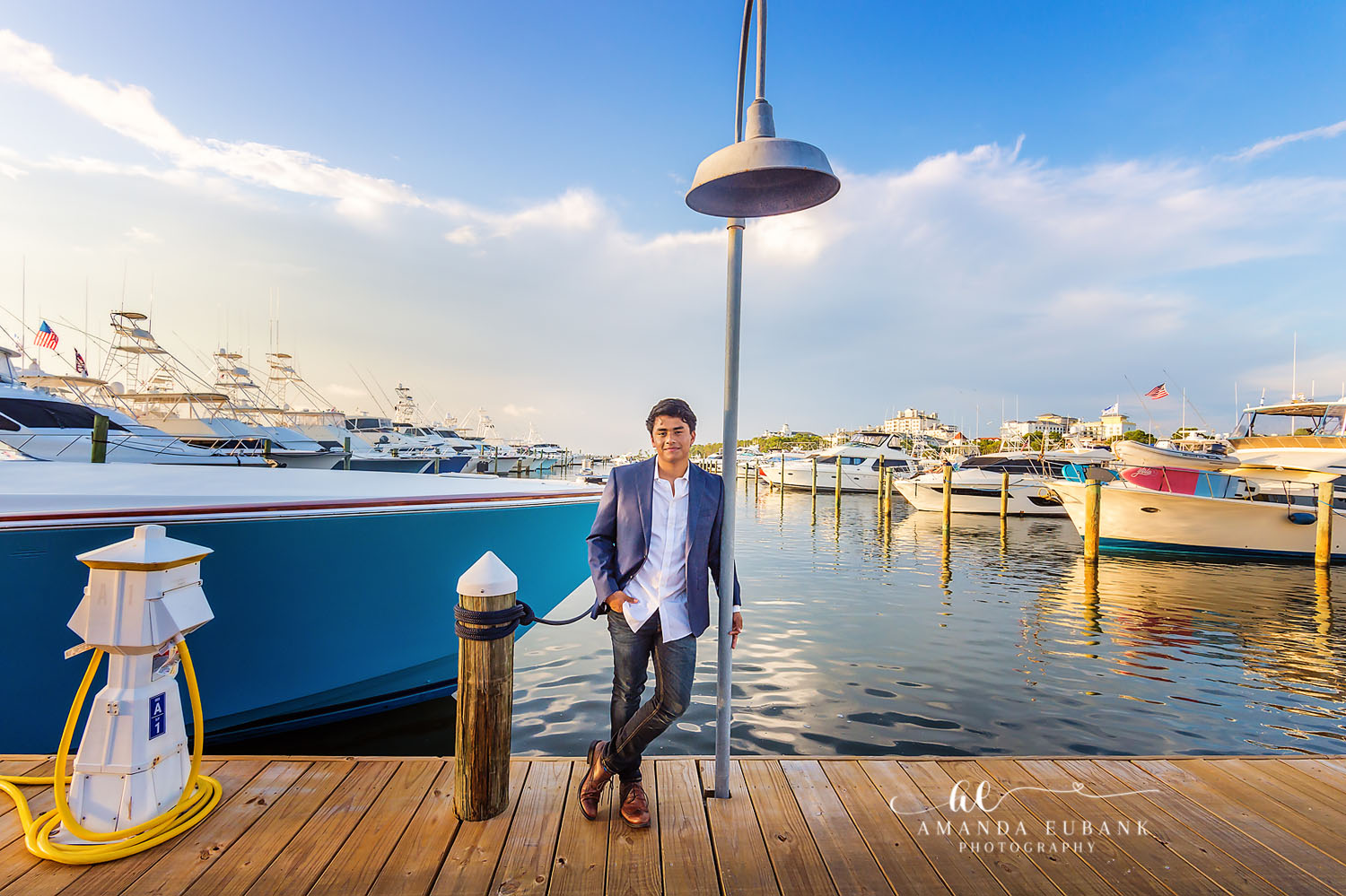 Seaside senior photographer captures male senior in blazer at marina dock with yachts behind