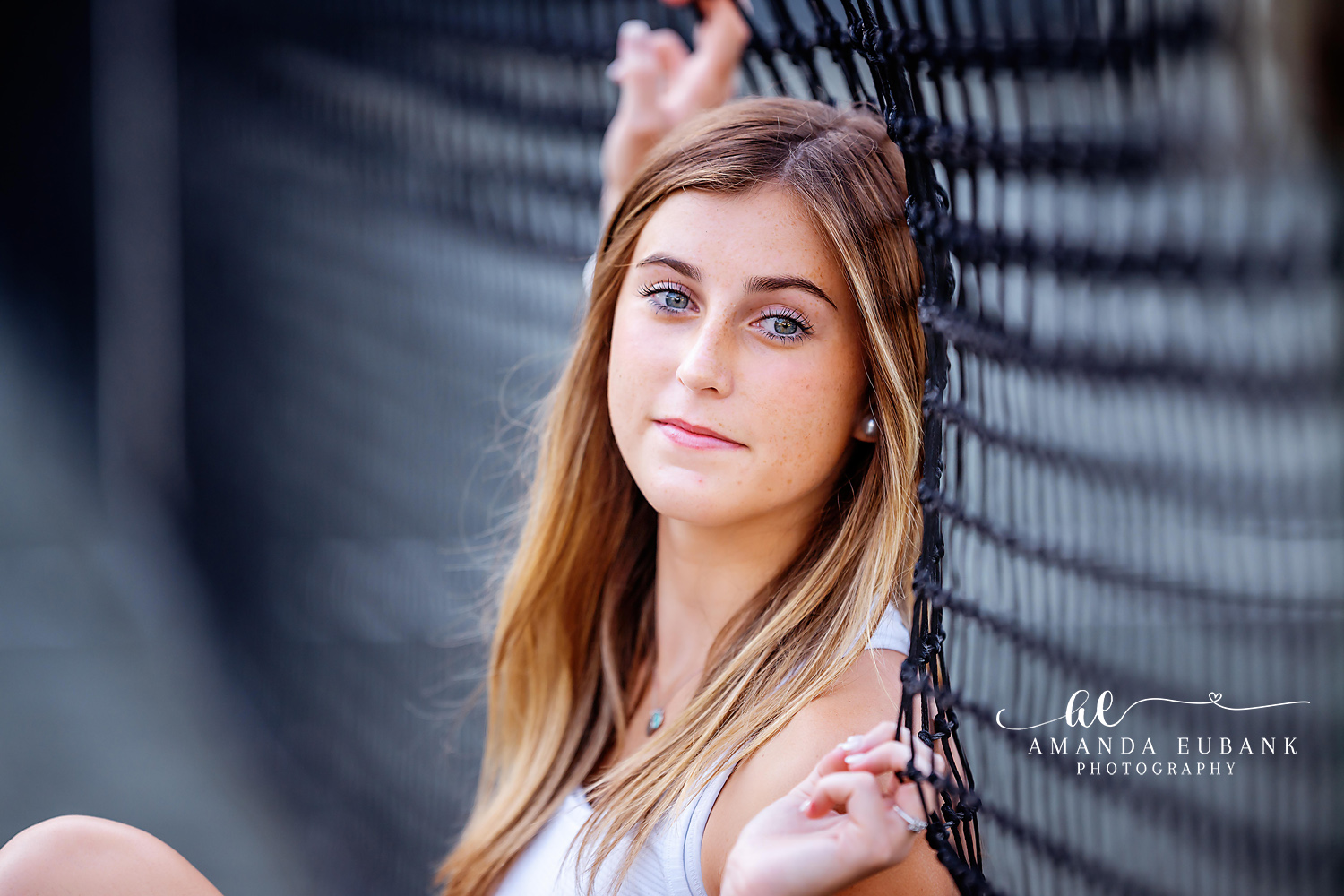 Seaside senior photographer captures close-up portrait of blue-eyed senior by a chain-link fence
