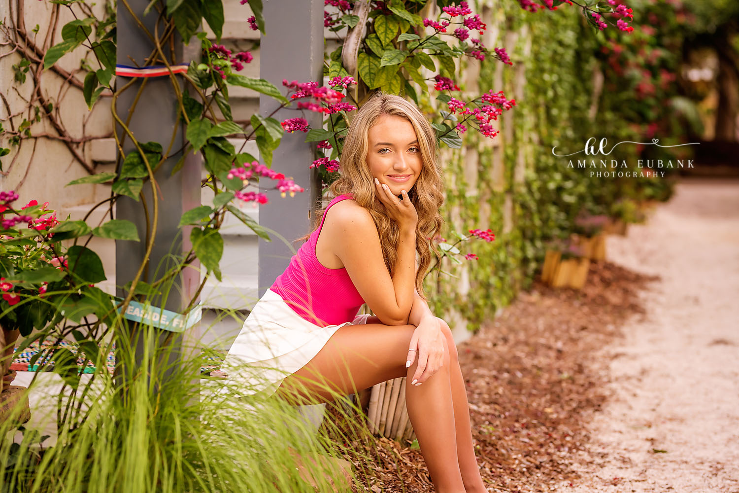 Seaside senior photographer captures senior posing by a wall with red bougainvillea blooms