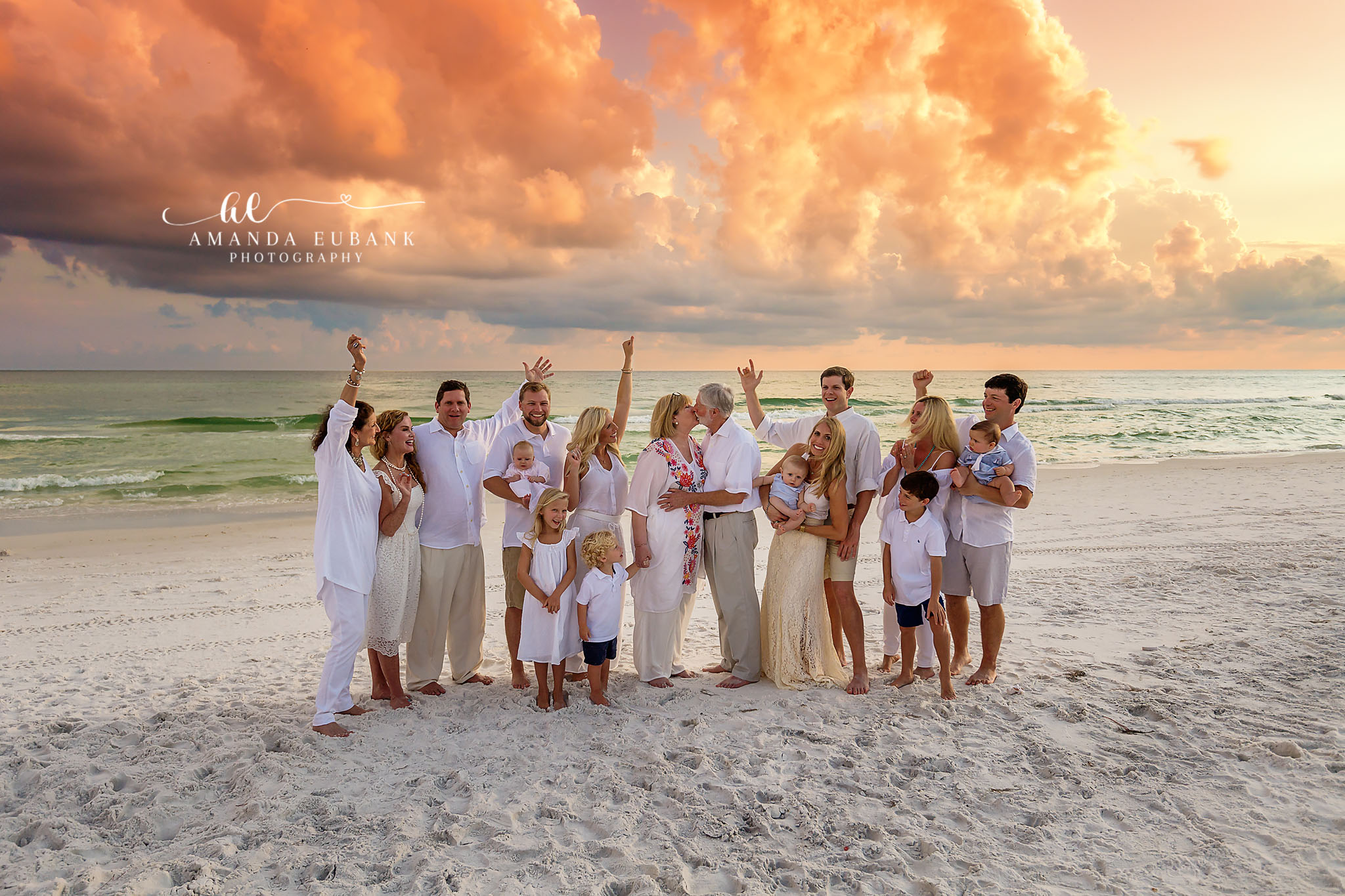 Seaside family photographer captures large extended family in all white celebrating at fiery sunset
