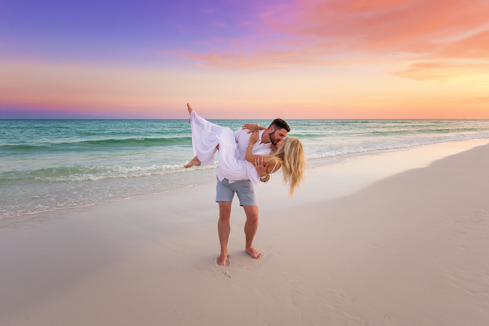 Couple standing on the beach at a dramatic blazing orange and deep red sunset with the sun on the horizon in Seaside Florida