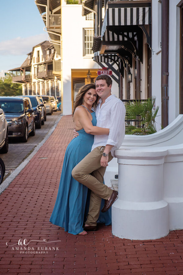 Engaged couple posing together and smiling on a charming brick street in the town of Seaside Florida with historic buildings in the background