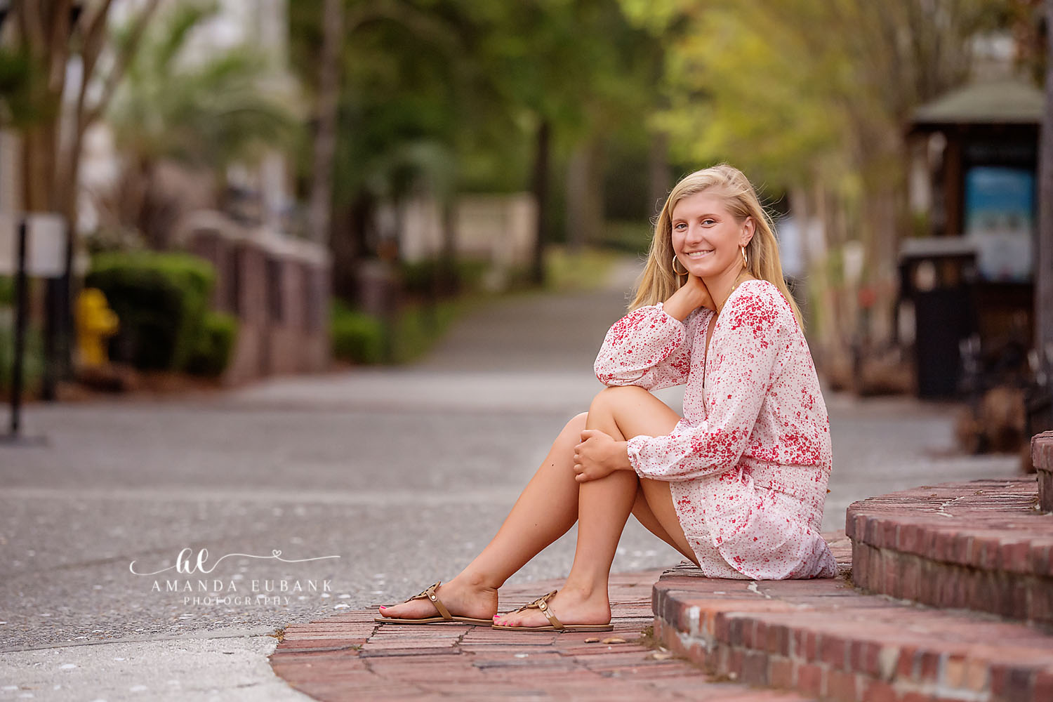 Seaside senior photographer captures blonde senior in red floral romper seated on brick steps downtown