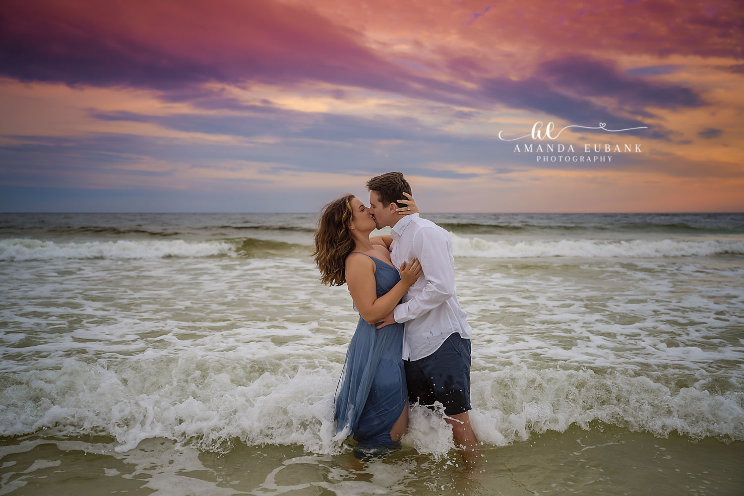Romantic engaged couple embracing on the beach at a warm golden hour sunset in Seaside Florida with ocean waves behind them
