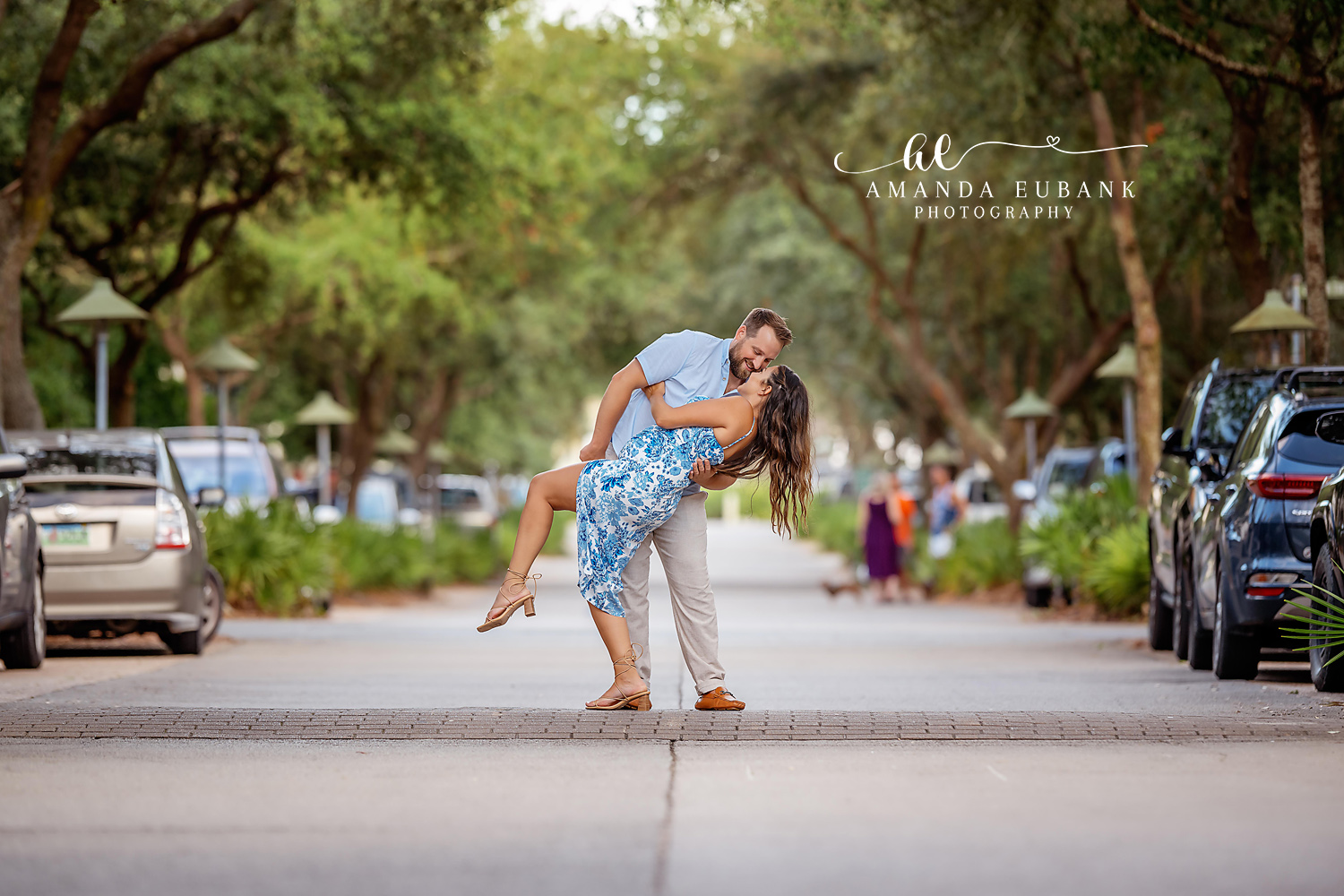 Man dipping woman and kissing her on a beautiful shaded tree lined avenue in Seaside Florida with lush green trees overhead
