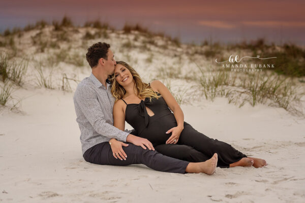 Pregnant woman in a blue gown and partner kissing during a Seaside Florida maternity portrait session
