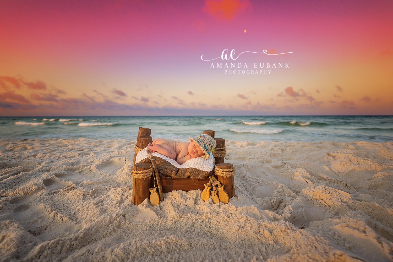 Newborn Photographer in Seaside FL | Coastal Newborn Session Newborn baby portrait by Seaside photographer with warm sunset sky and emerald Gulf water in background