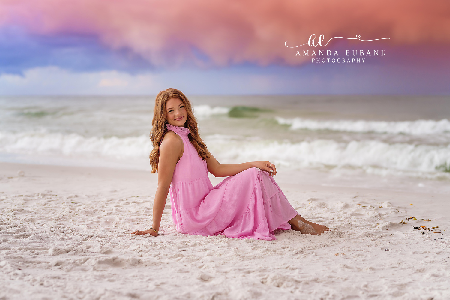 Senior girl with light brown hair in a blue dress at the beach at a warm golden and orange sunset sky in Seaside Florida