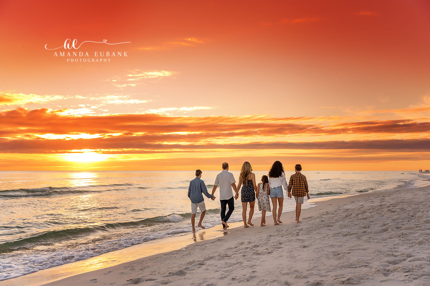Seaside family photographer captures family of five walking holding hands at fiery orange sunset