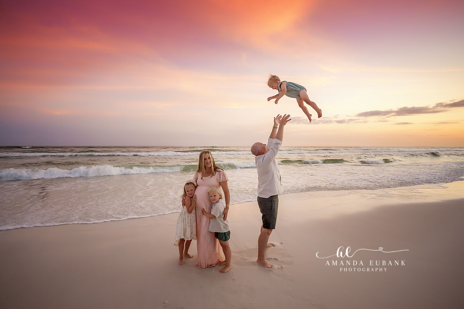 Seaside family photographer captures dad tossing baby in the air with family at sunset