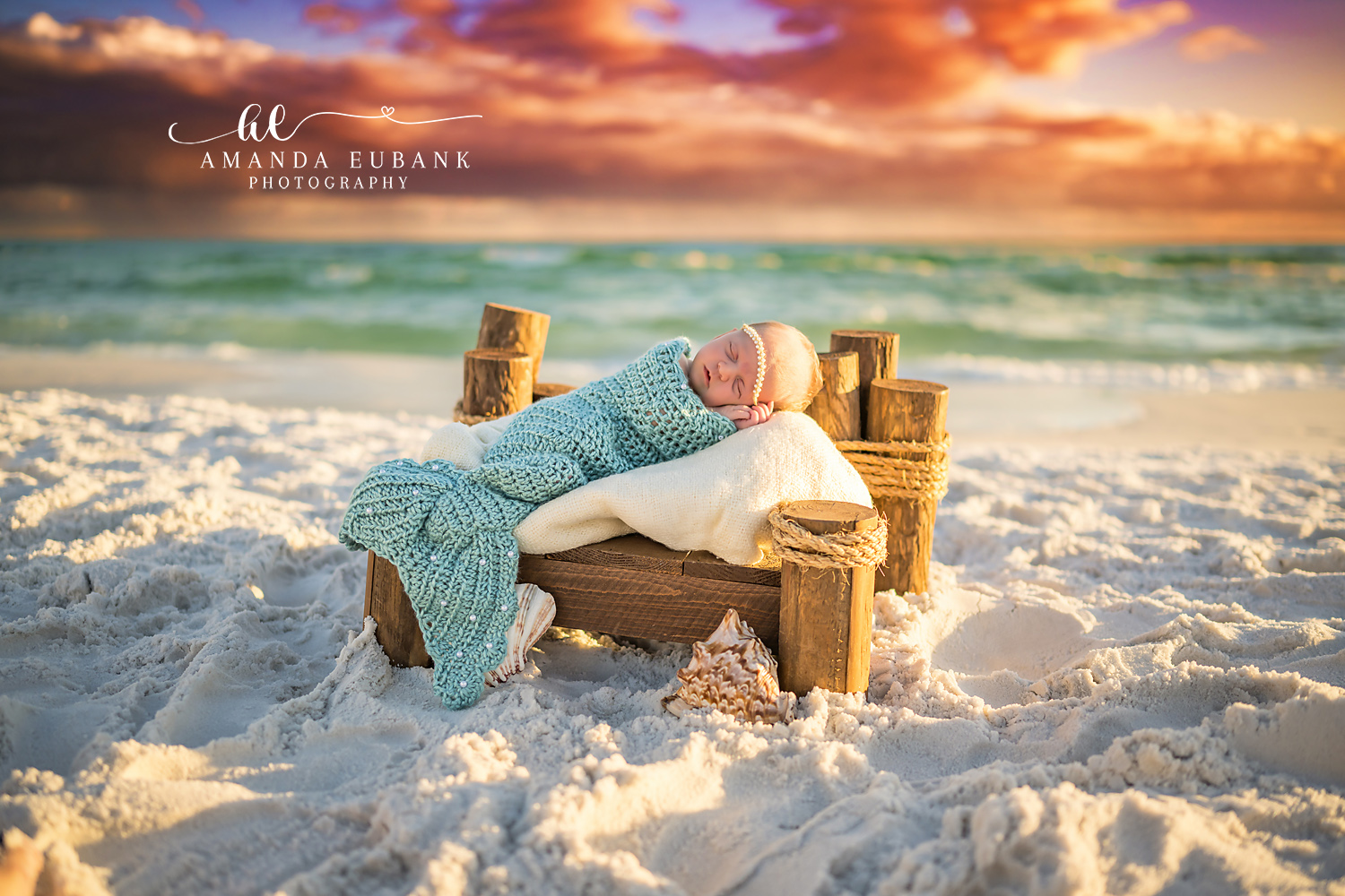 Seaside FL newborn photographer captures tiny sleeping newborn in soft pink wrap at a stunning beach sunset