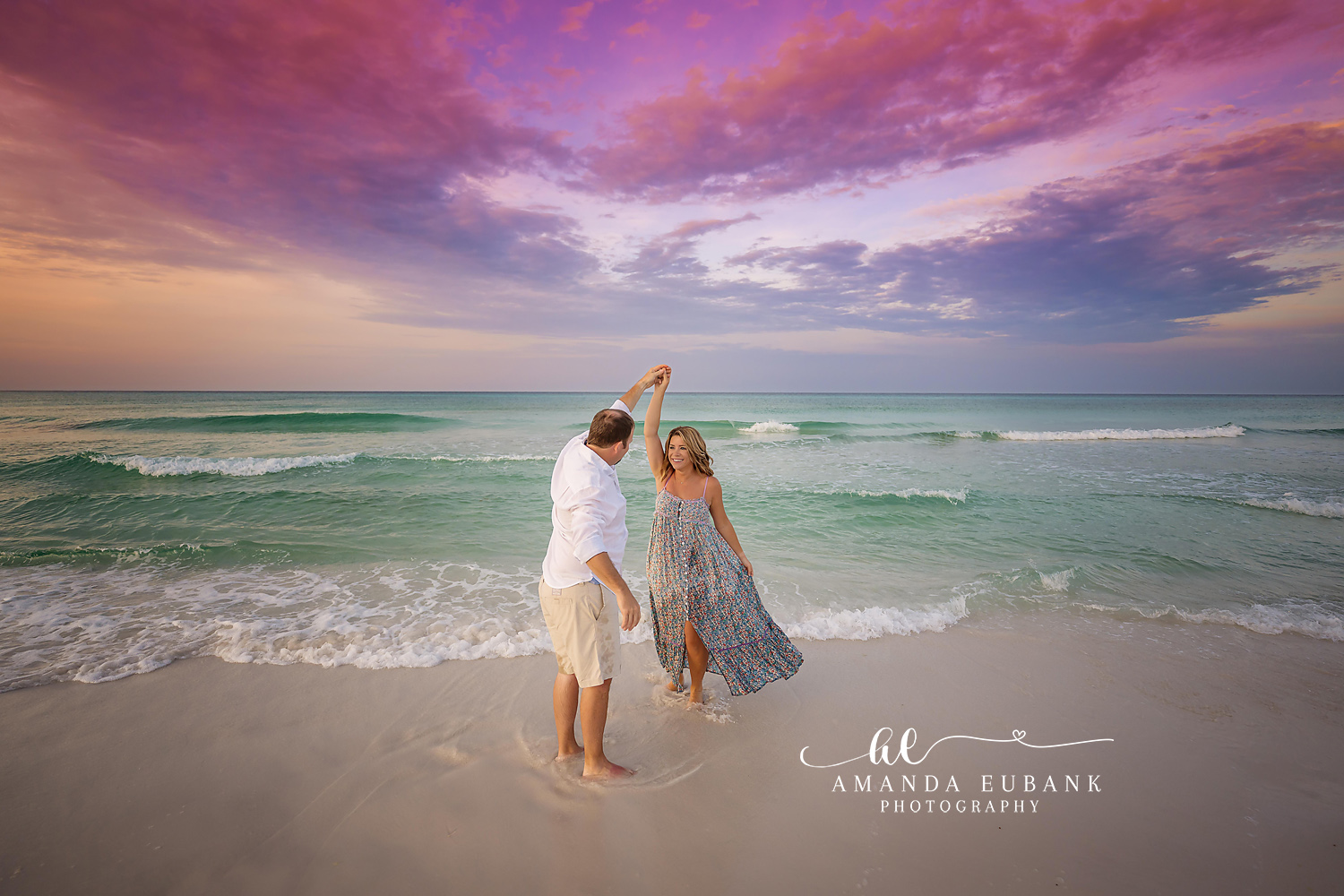 Engaged couple in a close romantic embrace on the beach at a warm and colorful sunset in Seaside Florida with the ocean nearby