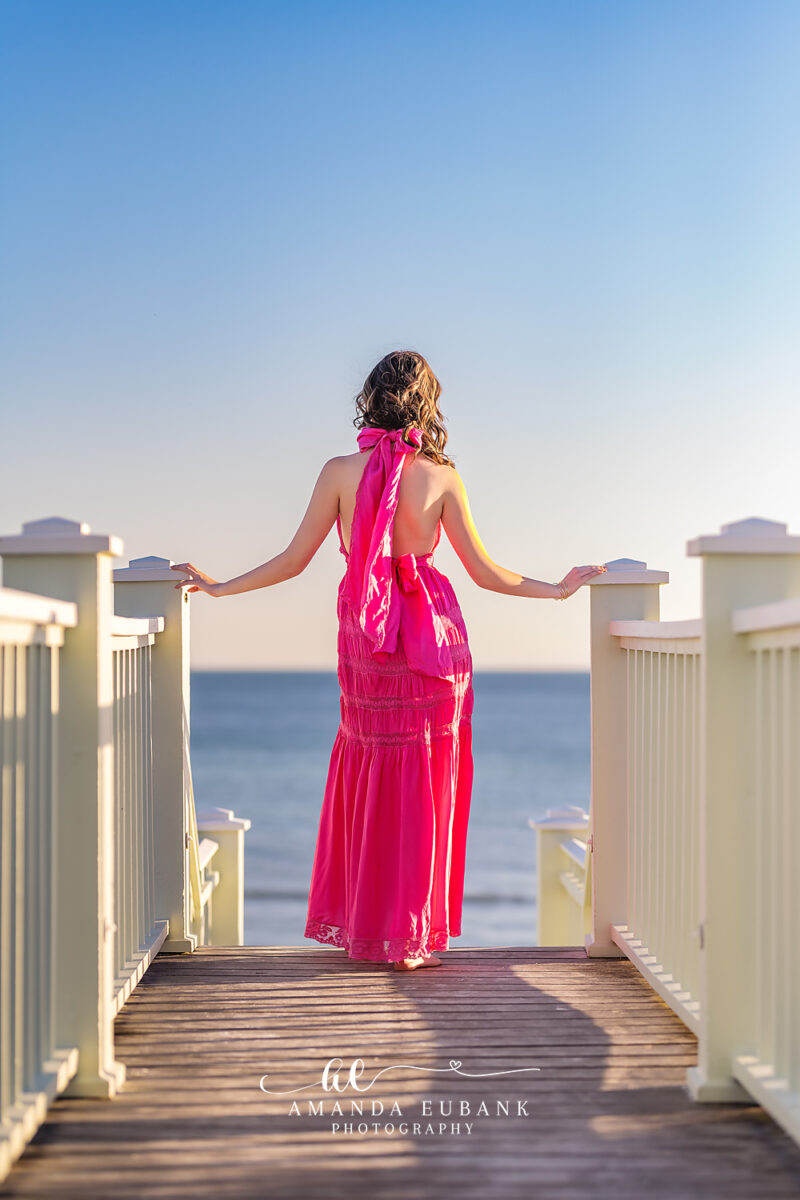 Senior girl with dark wavy hair in a colorful crochet top and skirt smiling at a beautiful outdoor setting in Seaside Florida