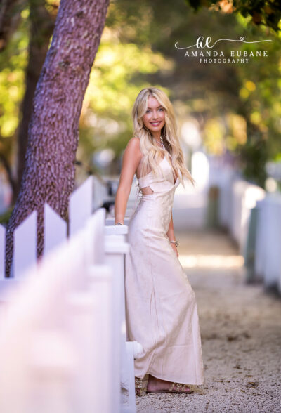 Senior girl with dark brown wavy hair in a blue maxi dress at the beach at a vivid multicolored sunset sky in Seaside Florida